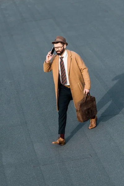 Handsome businessman with bag walking and talking on smartphone — Stock Photo