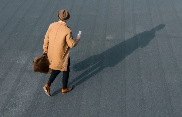 Visão traseira do homem de negócios com saco e smartphone andando no telhado — Fotografia de Stock