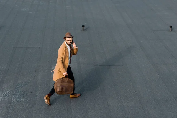 Hombre de negocios adulto con bolsa de cuero marrón caminando y hablando en el teléfono inteligente - foto de stock