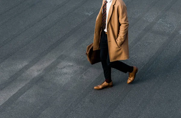 Vue partielle de l'homme d'affaires en manteau avec sac marchant sur le toit gris — Photo de stock