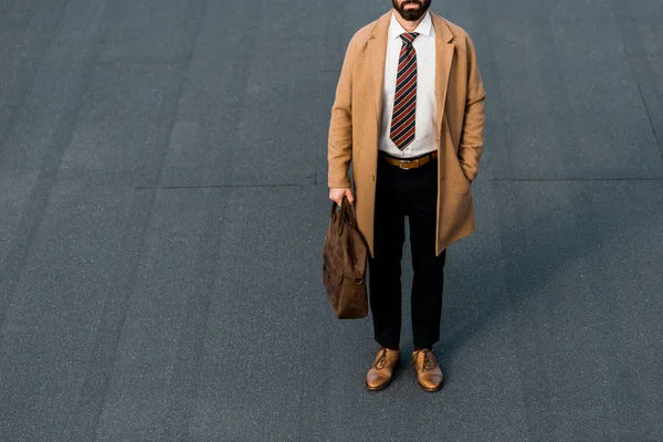 Vista ritagliata di uomo d'affari barbuto in piedi con borsa marrone in pelle — Foto stock