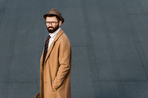 Vista laterale di uomo d'affari barbuto in piedi in cappotto con mano in tasca — Foto stock