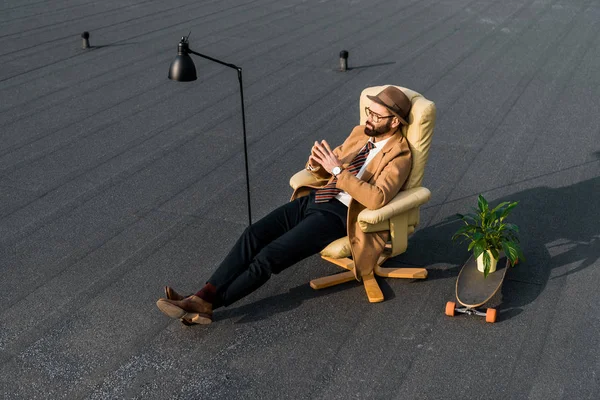 Bel homme d'affaires en manteau beige assis dans un fauteuil sur le toit — Photo de stock