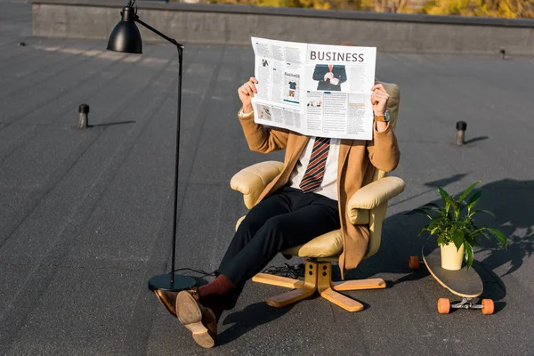 Hombre de negocios con cara oscura sentado en sillón y periódico de la celebración de negocios - foto de stock