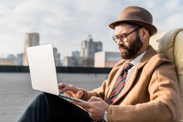 Handsome businessman sitting in armchair and using laptop — Stock Photo