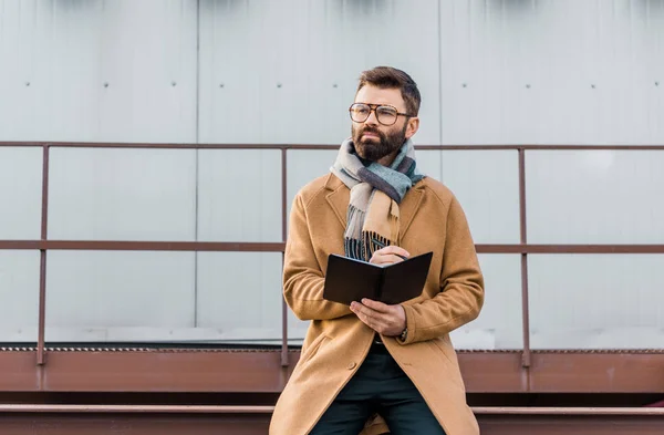 Empresário em pé de casaco e cachecol com caderno e caneta nas mãos — Fotografia de Stock