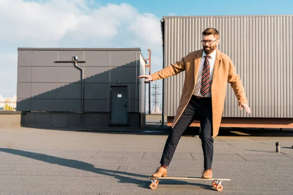 Cheerful businessman in suit and coat riding on penny board — Stock Photo