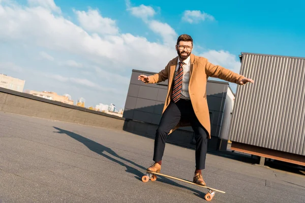 Bearded businessman in coat riding on penny board — Stock Photo