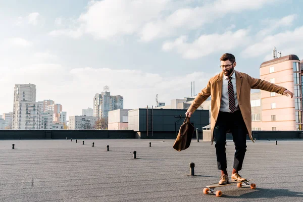 Handsome businessman riding on penny board on roof — Stock Photo