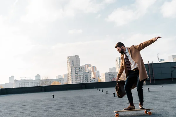 Side view of businessman in coat and formalwear riding on penny board — Stock Photo