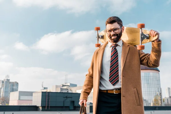 Alegre hombre de negocios sosteniendo penny board y sonriendo en gafas - foto de stock