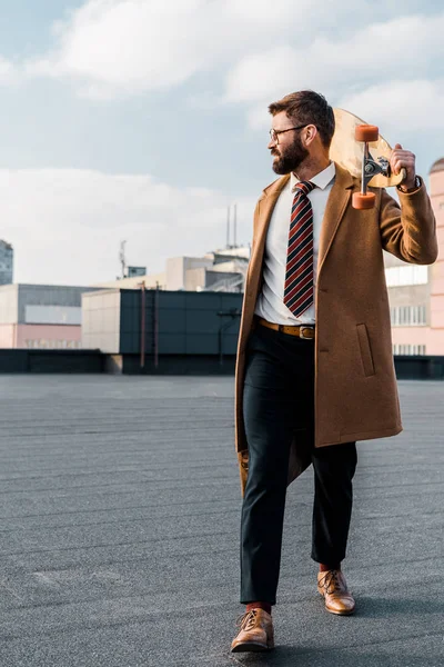 Successful businessman in formalwear and coat walking with penny board — Stock Photo