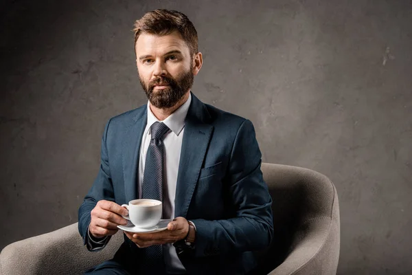 Hombre de negocios serio sentado en sillón con taza de café - foto de stock