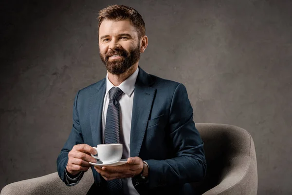 Hombre de negocios sonriente sentado en sillón con taza de café - foto de stock