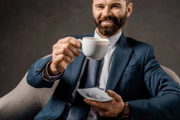 Messa a fuoco selettiva di tazza con caffè con uomo d'affari barbuto su sfondo — Foto stock