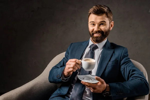 Homme d'affaires joyeux tenant tasse de café et assis dans le fauteuil — Photo de stock