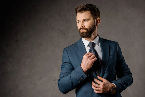 Confident bearded businessman standing in formalwear and touching tie — Stock Photo