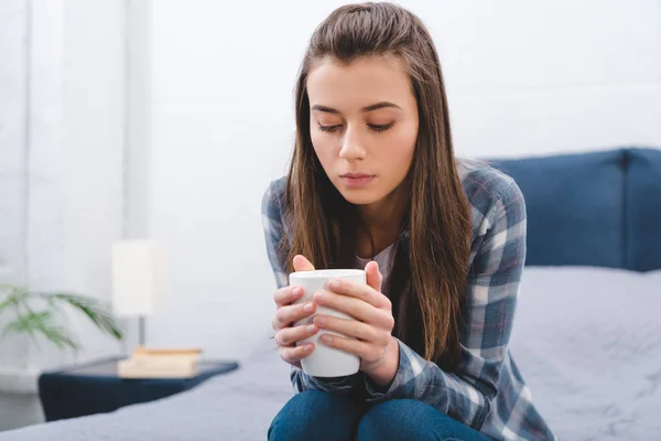 Schöne brünette Mädchen sitzt auf dem Bett und hält Becher mit Heißgetränk — Stockfoto