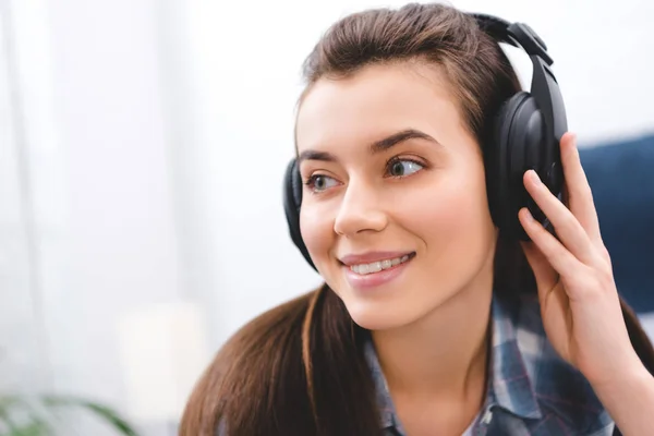 Hermosa mujer joven sonriente en auriculares mirando hacia fuera en casa - foto de stock