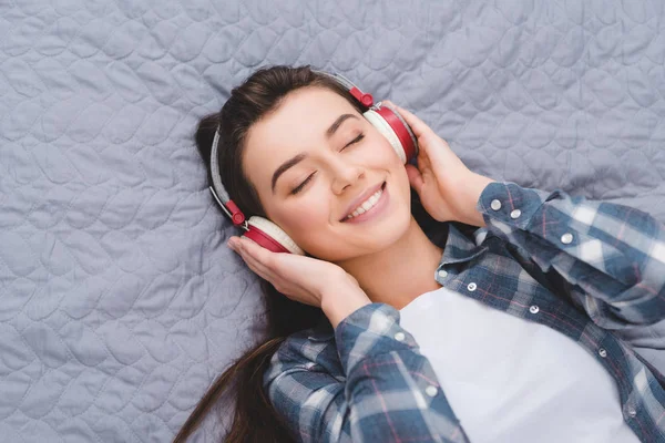 Schönes lächelndes Mädchen mit Kopfhörern auf dem Bett liegend — Stockfoto