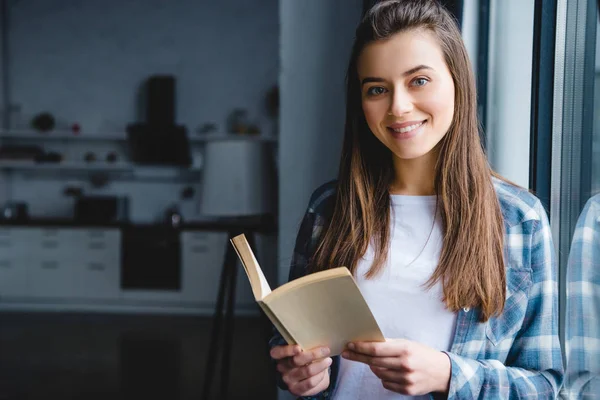 Schöne junge Frau hält Buch und lächelt in die Kamera — Stockfoto
