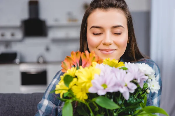 Schöne, glückliche junge Frau mit geschlossenen Augen, die zu Hause einen Blumenstrauß hält — Stockfoto