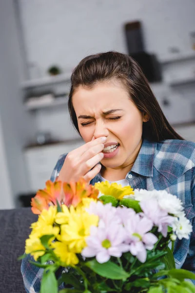 Girl with allergy sneezing and holding bouquet of flowers at home — Stock Photo