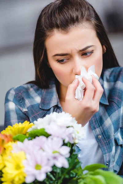 Jovem com alergia segurando tecido facial e olhando para flores — Fotografia de Stock