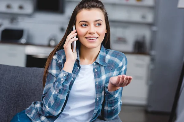 Улыбающаяся молодая женщина разговаривает по смартфону, сидя дома — стоковое фото