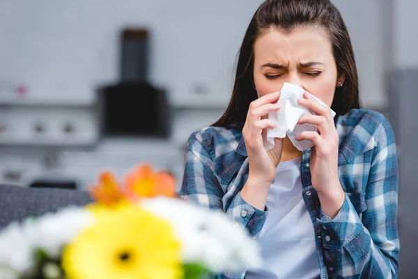 Молода жінка з алергією тримає тканину обличчя і чхає, квіти на передньому плані — стокове фото