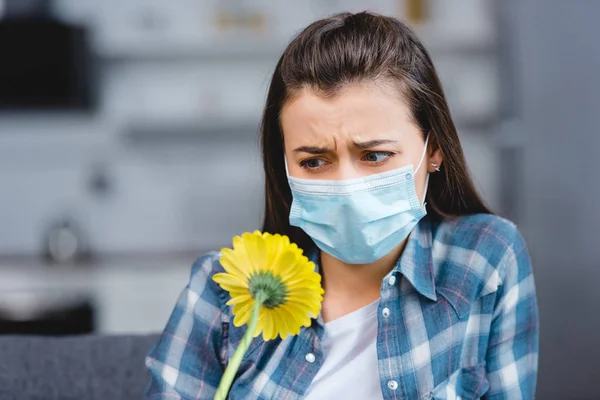 Junge Frau mit Allergie trägt medizinische Maske und blickt auf Blume — Stockfoto