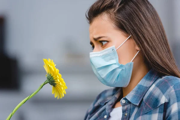 Seitenansicht einer jungen Frau mit Allergie, die eine medizinische Maske trägt und auf eine Blume blickt — Stockfoto
