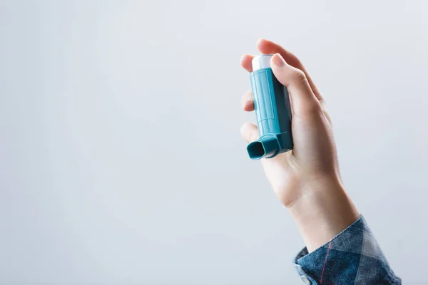 Vista parcial de cerca de una mujer joven que sostiene el inhalador aislado en gris - foto de stock