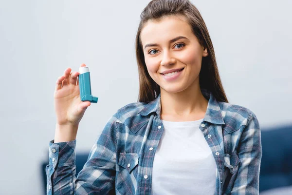 Feliz joven mujer sosteniendo inhalador y sonriendo a la cámara - foto de stock