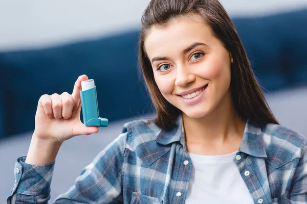 Feliz joven mujer sosteniendo inhalador y sonriendo a la cámara - foto de stock