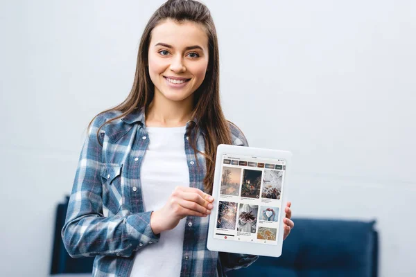 Happy girl holding digital tablet with pinterest app and smiling at camera — Stock Photo