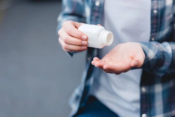 Tiro recortado de mujer joven sosteniendo contenedor con pastillas - foto de stock