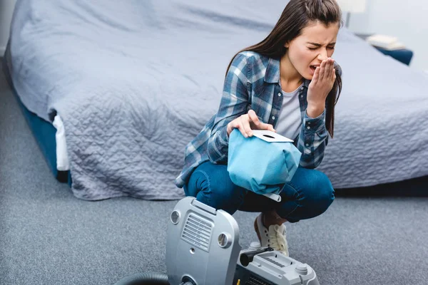 Vue grand angle de la fille avec des éternuements d'allergie tout en tenant le récipient de l'aspirateur avec de la poussière — Photo de stock