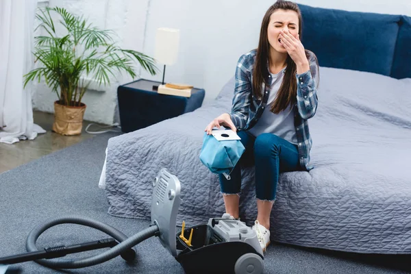 Frau mit Allergie-Auffangbehälter aus Staubsauger mit Staub und Niesen im Schlafzimmer — Stockfoto