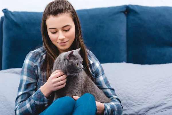 Glückliche junge Frau streichelt niedliche graue Katze im Schlafzimmer — Stockfoto