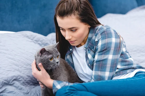 Beautiful young woman lying on bed with adorable british shorthair cat — Stock Photo
