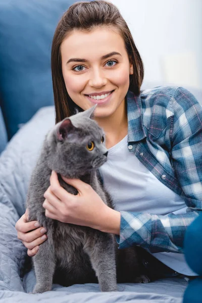 Schöne glückliche Mädchen umarmt Katze und lächelt in die Kamera im Schlafzimmer — Stockfoto