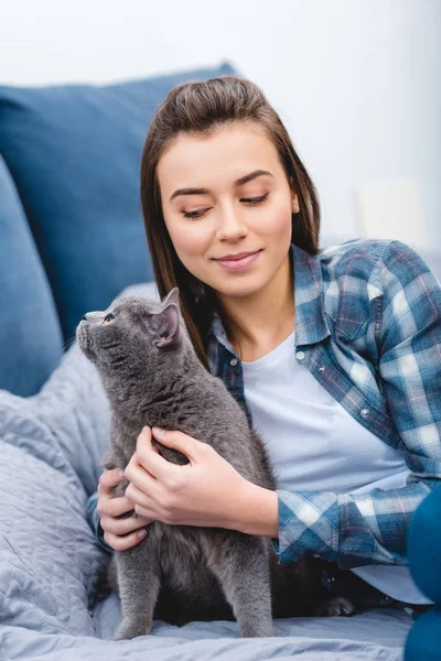 Belle fille souriante couchée sur le lit avec adorable chatte britannique à poil court — Photo de stock