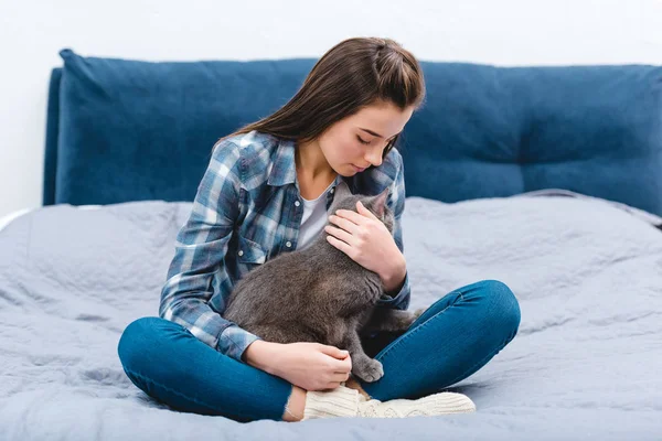Красивая молодая женщина, сидящая на кровати с милым британским короткометражным котом — стоковое фото