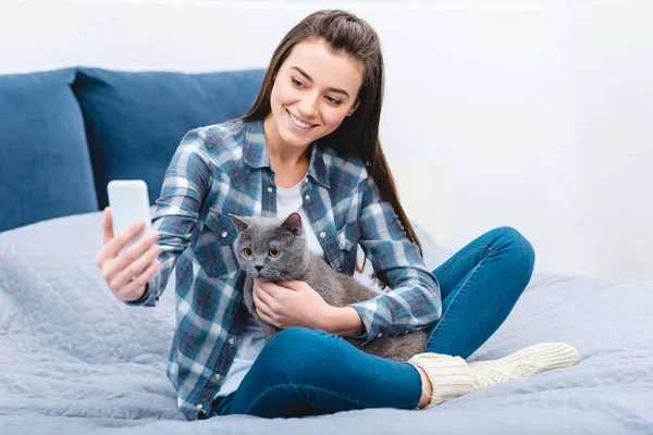 Sorrindo jovem mulher usando smartphone e tirar selfie com gato cinza bonito — Fotografia de Stock