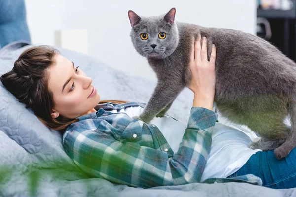 Jovem mulher deitada na cama com adorável gato cinza — Fotografia de Stock