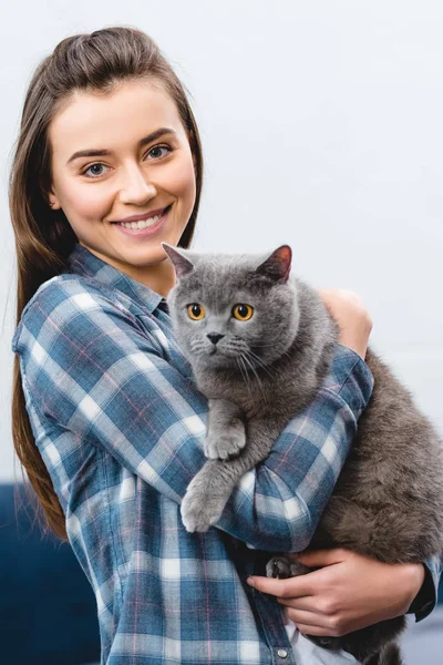 Jovem mulher segurando britânico shorthair gato e sorrindo para a câmera — Fotografia de Stock