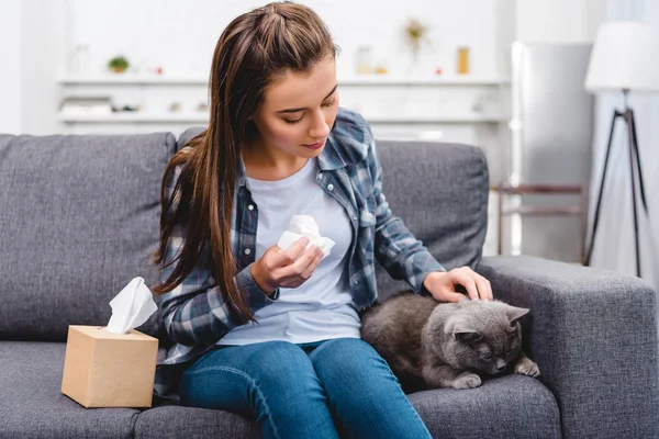 Girl with allergy holding facial tissue and stroking cat on couch — Stock Photo