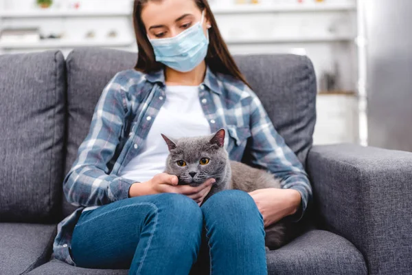 Mulher em máscara médica segurando gato e sofrendo de alergia em casa — Fotografia de Stock