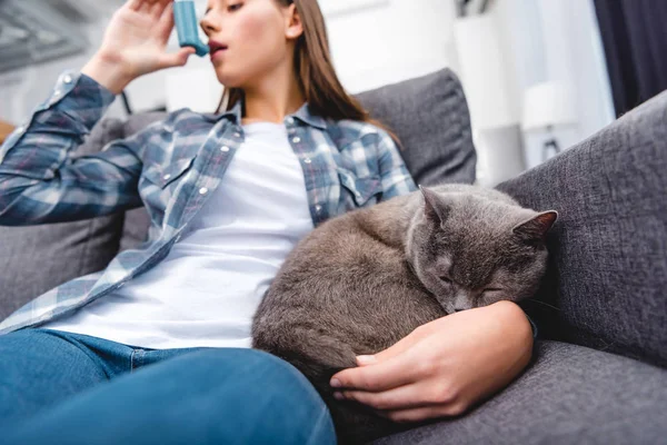 Низький кут зору жінки, використовуючи інгалятор, сидячи з кішкою на дивані — стокове фото